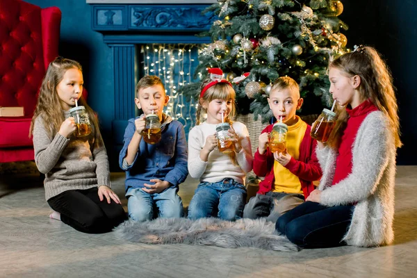 Vrolijk kerstfeest. Een groep kinderen op de achtergrond van een kerstboom, limonade drinken en glazen kloppen — Stockfoto