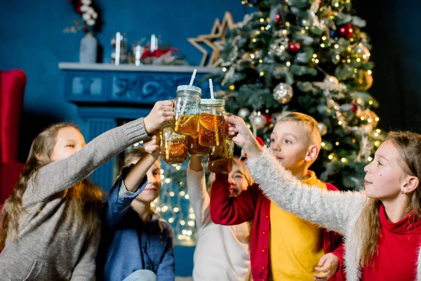 Groep van kinderen op de achtergrond van een kerstboom, limonade drinken en kloppen bril, focus op glazen — Stockfoto