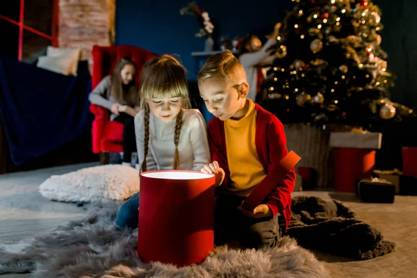 Gemütliches Zimmer im weihnachtlichen Stil eingerichtet. schöne Kinder sehen ein magisches Geschenk und bereiten sich auf den Urlaub vor. — Stockfoto