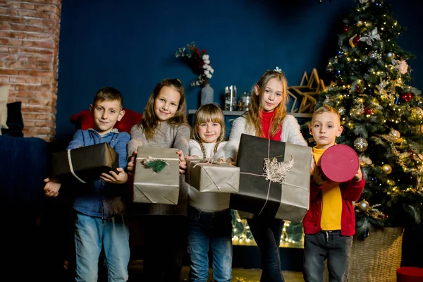 Joyeux groupe d'enfants tenant des cadeaux de Noël, sur le fond des décorations de Noël dans une belle chambre confortable . — Photo