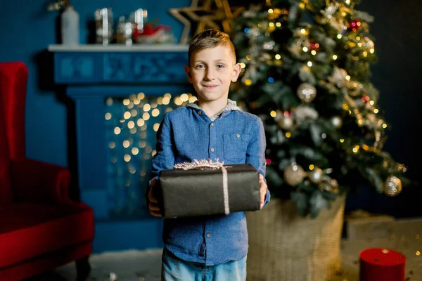 Beau petit garçon tenant un cadeau du Nouvel An sur le fond d'un arbre de Noël . — Photo