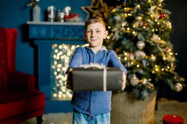 Beau petit garçon tenant un cadeau du Nouvel An sur le fond d'un arbre de Noël . — Photo