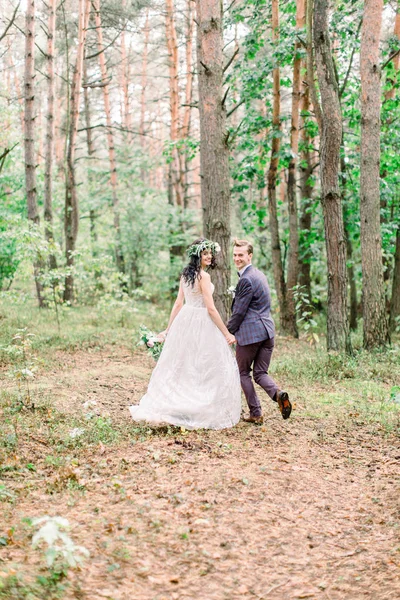 Zadní pohled na stylové venkovské dvojice novomanželů v jejich svatební den, procházky a běh v lese. Šťastná mladá nevěsta, elegantní ženich drží za ruce a baví — Stock fotografie
