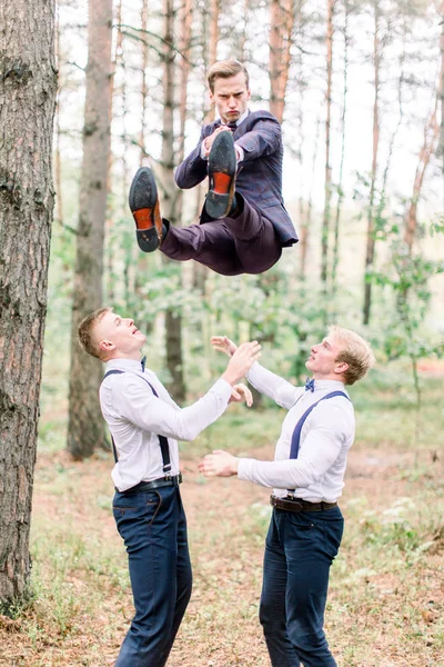 Przystojny pan młody i drużba dobrze się bawią i szaleją w lesie skacząc w dzień ślubu. — Zdjęcie stockowe