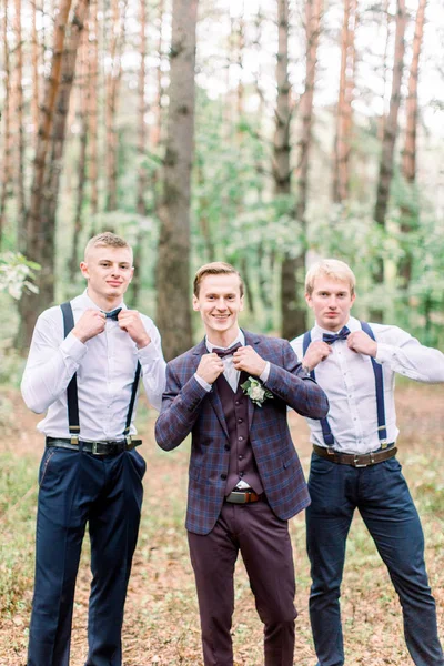 Pan młody stoi z przyjaciółmi w jesiennym lesie. Młody mężczyzna w eleganckim, kratowym garniturze i drużbach na sesji zdjęciowej ślubnej. — Zdjęcie stockowe