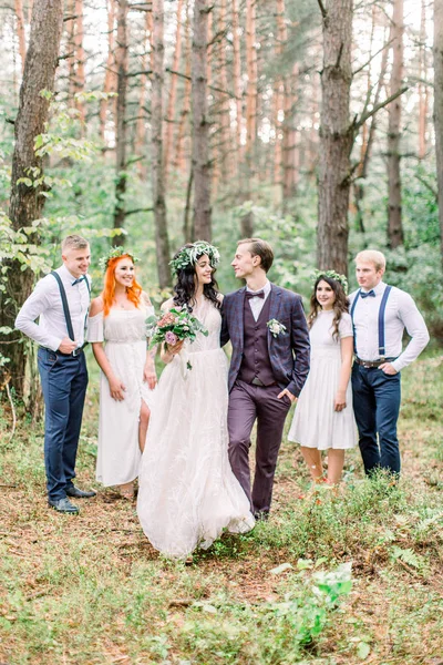 Счастливая пара с подружками жениха и невесты, позирующими на свадебной церемонии в лесу. Жених и невеста с лучшими друзьями позируют в сосновом лесу. Молодые люди веселятся. День свадьбы . — стоковое фото