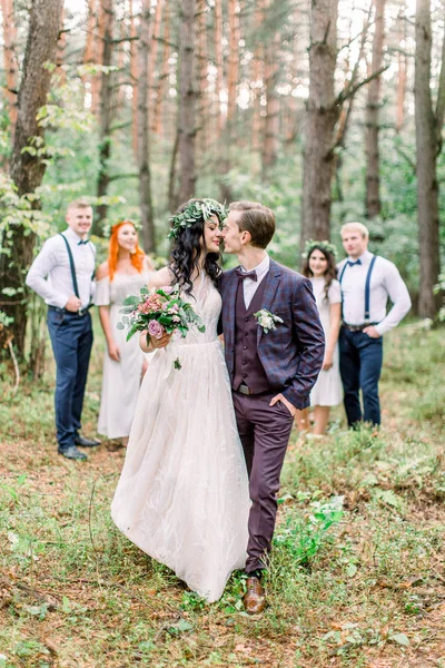 Líbající se novomanželé stojí před párem družiček a ženichů v lese. Svatba v rustikálním stylu venku — Stock fotografie