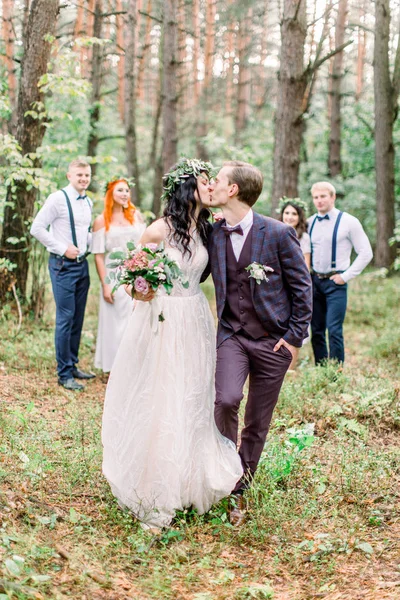 Стильные поцелуи невесты и жениха стоят перед парами подружек невесты и шаферов в лесу. Свадьба в деревенском стиле на открытом воздухе — стоковое фото