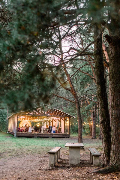 Stylish rustic restaurant wooden tent with wooden tables and chairs. Vintage design of the restaurant in the forest, decorated with lamps light bulbs. Wedding rustic outdoors