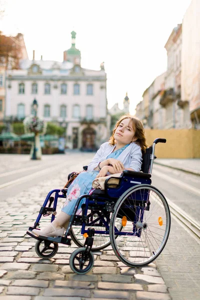Ein Mädchen in blauem Kleid im Rollstuhl draußen in der Stadt. der behinderte Mensch genießt das Leben. junge schöne behinderte Frau — Stockfoto