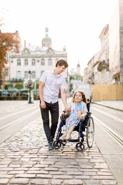 Junges Paar im Rollstuhl spaziert durch die Altstadt. Schönes Paar, Frau im Rollstuhl und ihr Mann, draußen in der Stadt — Stockfoto