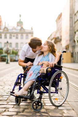 Şehirde yürüyün. Tekerlekli sandalyedeki neşeli kız, yakışıklı erkek arkadaşıyla öpüşürken birlikte zaman geçiriyor.