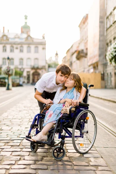 Glückliches Paar mit behinderter Frau, die in der Altstadt spazieren geht. Beziehungskonzept in Behindertenfragen mit Frau im Rollstuhl und jungem hübschen Mann — Stockfoto