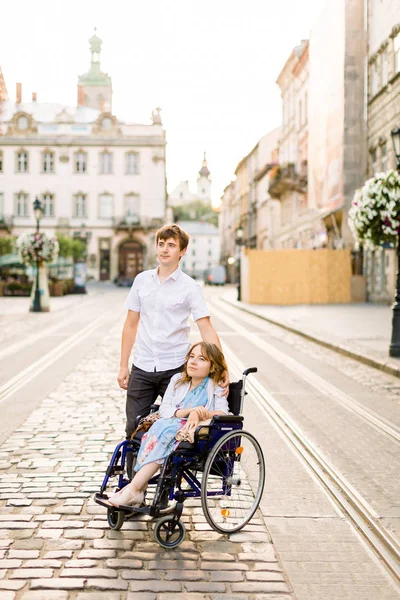 Junge Frau im Rollstuhl spaziert mit ihrem jungen hübschen Mann durch die Stadt — Stockfoto