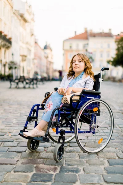 Ελκυστική ανάπηρη νεαρή γυναίκα με μπλε φόρεμα που κάθεται σε αναπηρική καρέκλα, σε εξωτερικούς χώρους στην πόλη — Φωτογραφία Αρχείου
