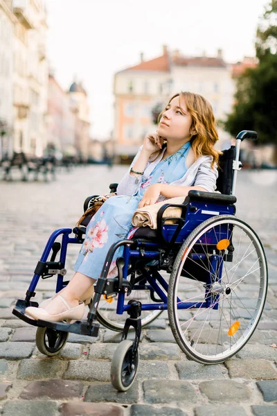 Attraktive behinderte junge Frau in blauem Kleid im Rollstuhl, draußen in der Stadt — Stockfoto