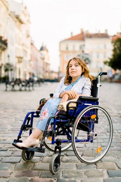 Glückliche junge Frau im Rollstuhl im Freien, posiert vor dem Hintergrund alter Gebäude in der Stadt — Stockfoto