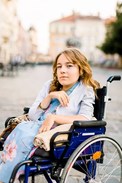 Πορτρέτο της νεαρής ξανθά μαλλιά γυναίκα κάθεται σε αναπηρική καρέκλα και κοιτάζοντας την κάμερα, το περπάτημα σε εξωτερικούς χώρους στο κέντρο της παλιάς πόλης — Φωτογραφία Αρχείου