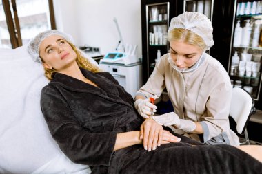 Doktor, bir kadının ellerinde hiperhidroz ve cildinde kırışıklıklara karşı botulinyum toksini enjekte eder. Kadın kozmetolojisi, cilt bakımı.