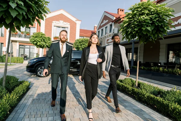 Dynamic Business team, Caucasian woman and man, African man, hurry to outdoor meeting, black car and modern office buildings on the background