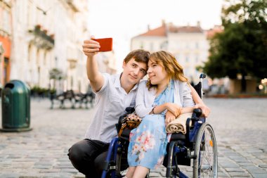 Mutlu çift, eski şehrin arka planında tekerlekli sandalyedeki kadınla selfie çekiyor..
