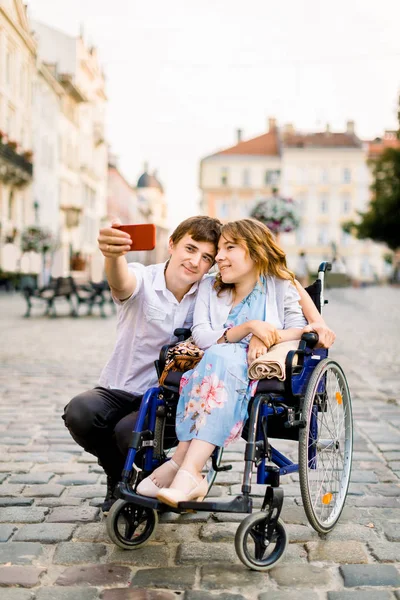 Junge Frau im Rollstuhl und ihr Mann beim Selfie im Freien in der Altstadt — Stockfoto