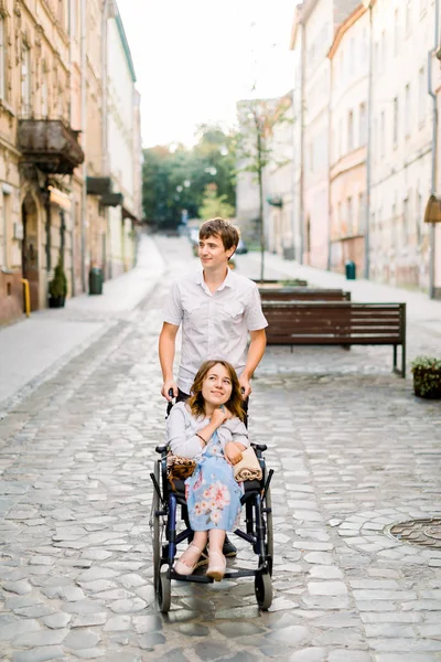Mutlu, tekerlekli sandalyedeki güzel kadın ve güneşli bir günde yaşlı şehir merkezinde genç yakışıklı bir adam.