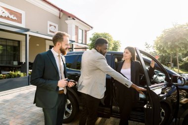 Mutlu müşteriler açık havada araba galerisinde ayakta duran yeni bir araba satın alıyorlar. İş kıyafetleri içinde iki adam yeni bir araba seçerken, genç ve güzel bayan satış müdürü açık kapının yanında duruyor.