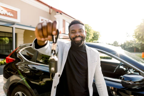 Potret penjual mobil Afrika memegang kunci mobil. Pria muda Afrika yang ceria dan ceria tersenyum menunjukkan kunci mobil untuk mobil barunya berpose di luar ruangan di salon dealer — Stok Foto