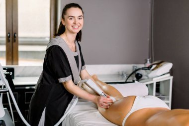 Modern kaplıca merkezindeki bayan müşterisi için popo masajı yapan genç, gülümseyen bir kozmetik uzmanı..