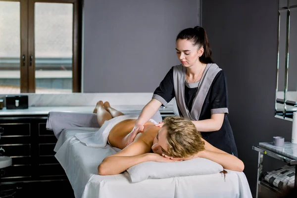 Young woman lying on a massage table, relaxing, getting professional manual back massage. Young woman masseur doing massage on woman back in medical center