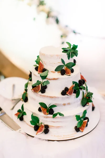 Wedding rustic cake with figs, and berries with a white cream. On the table in a cafe outdoors.
