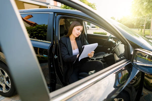 Affärskvinna sitter i bilen med anteckningsbok prata på mobiltelefon och göra anteckningar på papper. Kvinnlig chef arbetar i lyxbil. — Stockfoto
