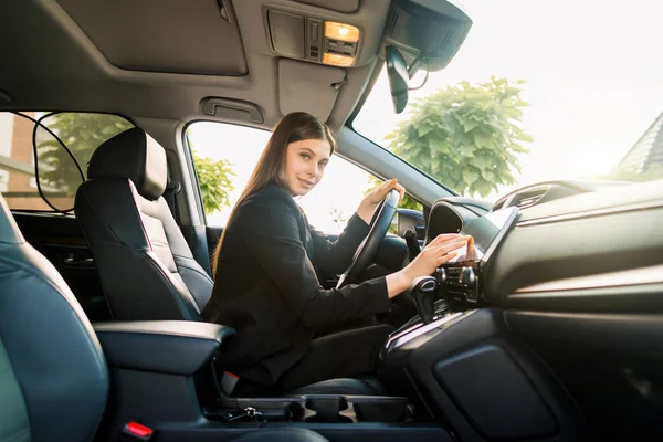 Beautiful smiling young woman in black business suit driving car, attractive girl sitting in automobile, outdoors summer portrait. — 스톡 사진