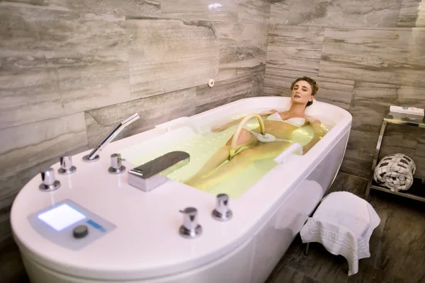 Ung kvinna njuter av hydromassage i bubbelbad med grönt ljus. Avslappnad kvinna att få hydromassage i professionella spa center — Stockfoto