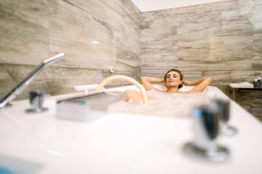 Spa kliniğinde hidroterapi görürken küvette yatan gülümseyen genç bir kadın.