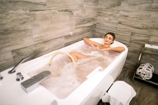 Zdravé lázně. Mladý kavkazský krásný relaxační žena ležící ve vaně s hydromasáží. — Stock fotografie
