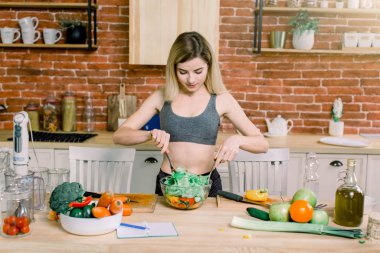 Yeni mutfakta yemek pişiren bir kadın sebzelerle sağlıklı yemekler yapıyor. Yirmili yaşlarda beyaz bir kadın.