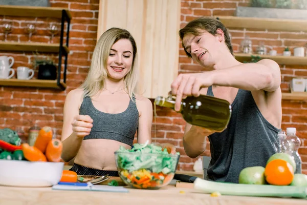 diet, healthy eating, fitness lifestyle, proper nutrition. health conscious couple cooking low calorie dinner in home kitchen. A man pours olive oil into a salad