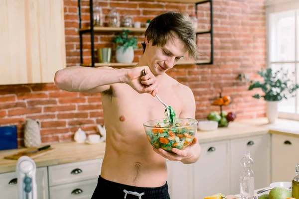 Its so delicious. Casual happy young man preparing salad at home in loft kitchen and smiling. — Stock Photo, Image