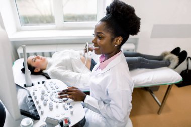 Gülümseyen Afrikalı kadın doktor pratisyen kadın karnını modern ultra ses ekipmanları kullanarak kontrol ediyor.