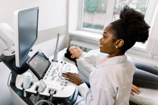 Young African female doctor using ultrasound machine in clinic, makes abdominal ultrasound for pregnant woman patient. Ultrasound Scanner. Sonography. — Stock Photo, Image