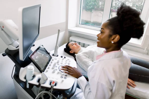 Primer plano de la sonógrafa médica africana escaneando el vientre de las mujeres embarazadas jóvenes con transductor ultrasónico haciendo ultrasonografía obstétrica — Foto de Stock