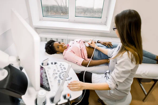 Diagnóstico ultra-sonográfico do estômago em abdominal para jovem mulher africana. O médico passa o sensor de ultra-som sobre a barriga dos pacientes e trabalha no painel do scanner. Diagnóstico de órgãos internos . — Fotografia de Stock