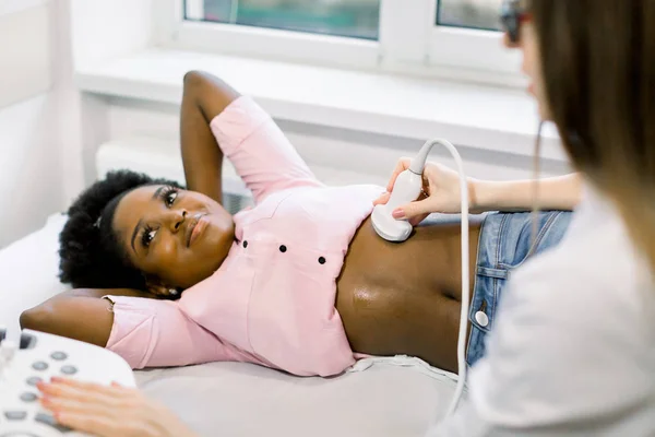 Ultraschallgerät in der Hand eines professionellen Arztes, der eine junge schwangere Patientin in Afrika untersucht und Ultraschallsonographie des Bauchraums durchführt — Stockfoto