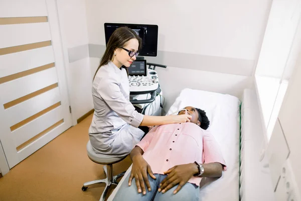 Junge afrikanische Patientin während der Ultraschalluntersuchung einer Schilddrüse, die auf dem Sofa in der Arztpraxis liegt — Stockfoto