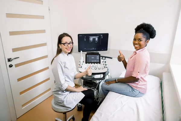 Porträt einer lächelnden Ärztin und glücklichen Patientin, die in die Kamera blickt und nach dem Ultraschalltest die Daumen nach oben zeigt und über die Ergebnisse spricht. — Stockfoto