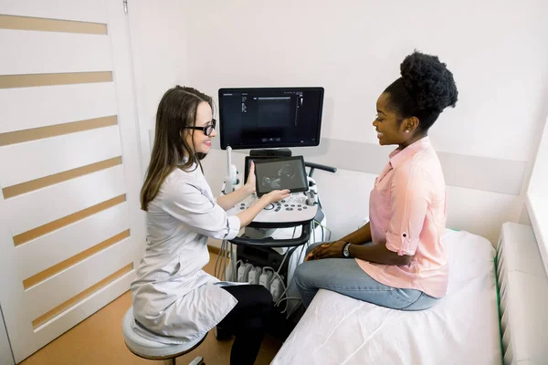 Professionelle Ärztin gibt Ratschläge für die Patientin junge schwangere afrikanische Mädchen nach Ultraschall, zeigt die Tablette mit dem Foto eines Babys — Stockfoto