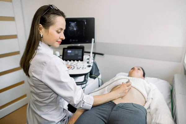 Jovem mulher grávida caucasiana submetida a ultra-som abdominal na clínica — Fotografia de Stock