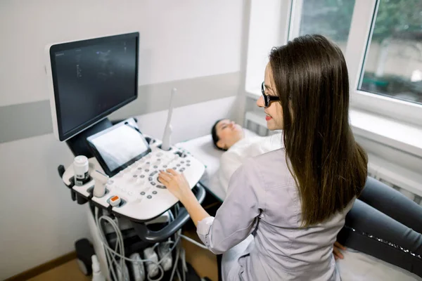 Вид сбоку молодой женщины-врача в белом халате, проводящей ультразвуковое обследование живота пациентке . — стоковое фото